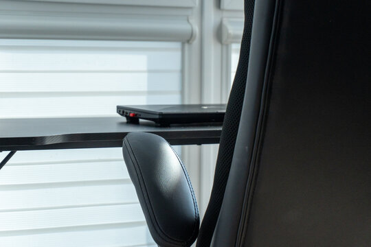 Chair and laptop positioned on a sleek desk near a window in a modern workspace during daylight hours