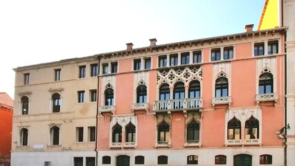 Venetian Gothic facade with pink walls and ornate white stone tracery. Arched windows and balconies with intricate detailing create a symmetrical, elegant composition—capturing timeless architectural 