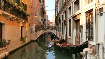 Charming canal scene in Venice with a small arched bridge and colorful facades. A gondola rests by...