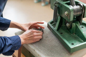 A woman makes holes in a leather belt in a workshop.