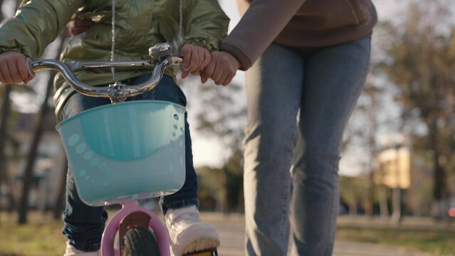 mother teaches little child to ride bike in the city, kid rides on sidewalk, happy family, baby plays and laughs with mom, learn ride, make childhood dream come true girls, daughter and mom are funny. - Powered by Adobe