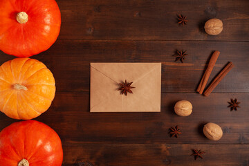 Flat lay of pumpkins with craft envelope, walnuts, cinnamon sticks and star anise on rustic wooden table. Seasonal autumn composition perfect for Thanksgiving, harvest, and fall greeting cards.