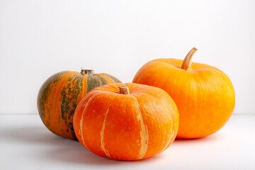 Three pumpkins on a white background. Autumn harvest, seasonal vegetables, and natural food concept. Perfect for fall, Halloween, Thanksgiving, eco lifestyle, healthy diet, and festive decor visuals.