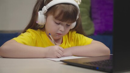 little schoolboy student writes mathematics notebook. child kid solves difficult learning problems. child education program. girl headphones with digital laptop writes notebook. study work home desk - Powered by Adobe