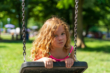 portrait of adorable beautiful little girl swinging gently leaning on the seat of a swing in a...