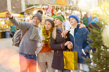 Portrait of positive family of four visiting Christmas street fair, pointing to something