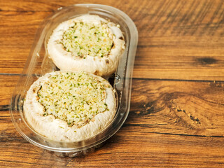 Two stuffed mushrooms in a plastic package on wooden background. Fine meal made of natural ingredients. Agriculture and farming, Food industry