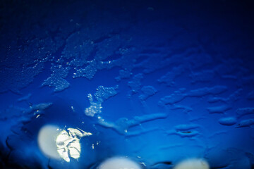 Car front glass covered with frosted ice and defrosted path with blue sunrise sky and warm city lights. Cold winter scene. Driving in dangerous conditions concept.