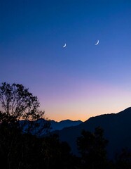 Two crescent moons hang in a twilight sky above a silhouetted mountain range