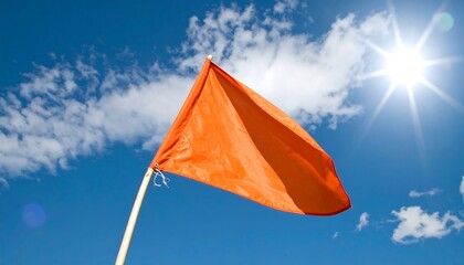 An orange warning flag billows against a vibrant, clear blue sky with fluffy white clouds and a bright sun.