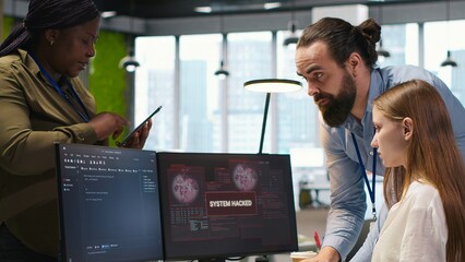 Young programmer in office requests help from IT experts detecting and blocking hacker intrusion. Intern assisted by staff members coordinating incident response for network attack, camera A