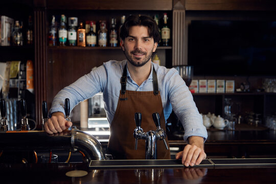 A man brewer is standing behind a bar counter, serving customers