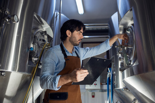 A man wearing an apron is diligently working hard in a brewery - Powered by Adobe