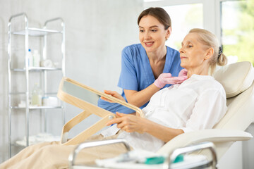 Obraz premium Old woman patient lying on clinical chair discussing face aesthetic procedures with doctor