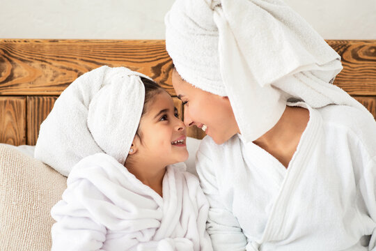 Closeup portrait of loving young mother and cute little daughter in bathrobes sitting on bed and bonding after shower, enjoying time together at home. Positive family having beauty day at hotel