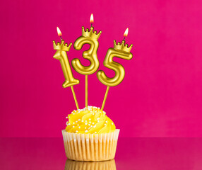 Birthday celebration with number 135 candle - Yellow cupcake on a pink background