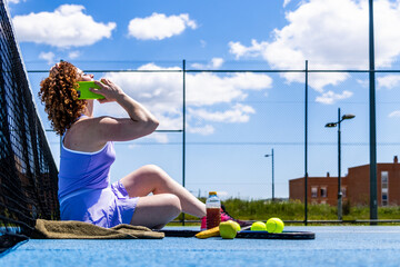 Female tennis player relaxing courtside during training break, making phone call