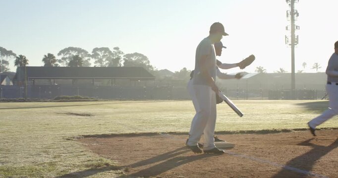 3 male baseball teammates carrying bat and gloves entering first base at dawn, practicing defense