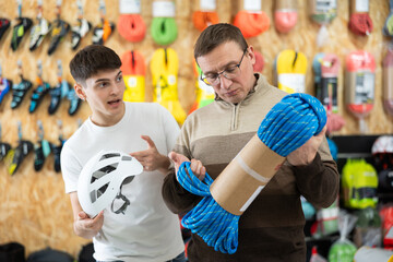 Father and adult son carefully select climbing equipment for a hike in a sports equipment store