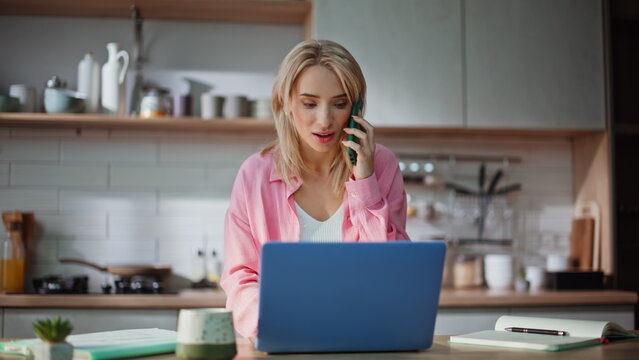 Multitasking freelancer talking smartphone typing laptop at kitchen closeup