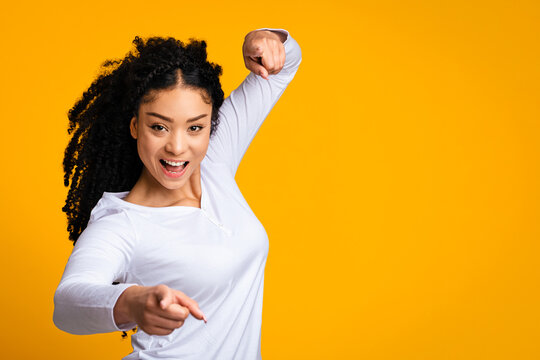 Gotcha. Excited beautiful african american woman pointing at camera with two hands, indicating somebody, shouting hey you, cheerful black lady having fun over yellow studio background, copy space