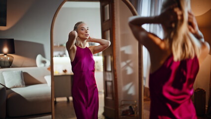 Fototapeta premium Joyful lady trying dress admiring stylish look in living room mirror closeup