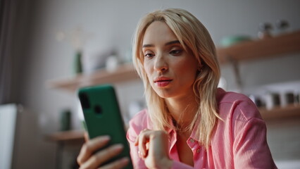Blonde lady shopping online smartphone choosing goods alone at kitchen closeup