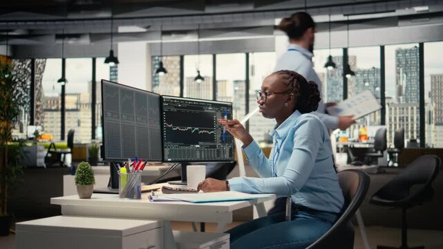 Financial analyst in prop firm office doing research on stock market shares. Brokerage company professional reading investment analysis reports on computer monitor to make trading decisions, camera A