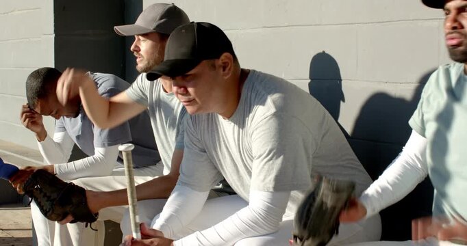 Tossing baseball senior coach prompting diverse team preparing in dugout, gripping gloves and bat