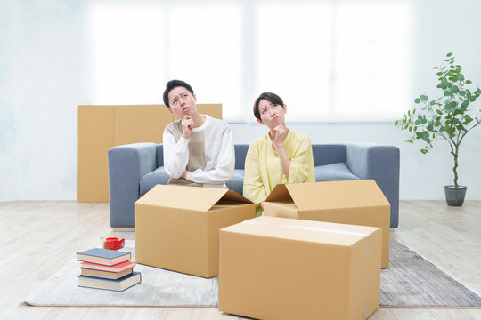 困った表情でダンボールを整理するカップル - Powered by Adobe