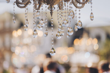 Luxurious crystal chandeliers in the middle of a forest in the glow of the sunset. Fabulous wedding decor with chandeliers. Decorating a with antique chandeliers. Light bulb in the shape of a candle.