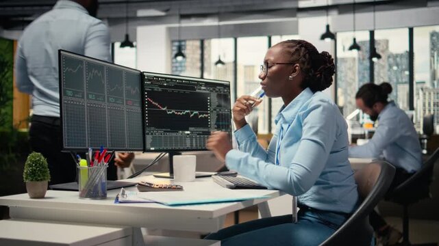 Forex expert in office looking over candlestick charts on screen to assess stock market volatility. African american woman in hedge fund company reading investment reports, camera A