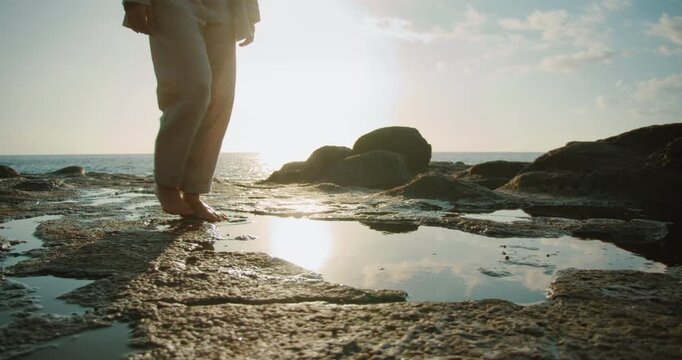 Barefoot woman walking on rocky shore with tide pools during golden hour