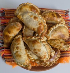 Freshly baked argentine empanada pasties on colorful striped fabric napkin and white wooden background