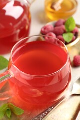 Tasty raspberry tea in glass cup, teapot, berries, honey and mint on table, closeup