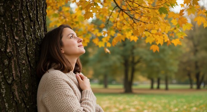 Woman leaning against tree gazing at golden autumn leaves in park, gentle natural light style, concept of mindfulness gratitude and seasonal change, great for wellness promos counseling services