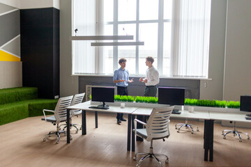 two young businessmen in business clothes talking during break in office, office workers working together and communicating, general plan