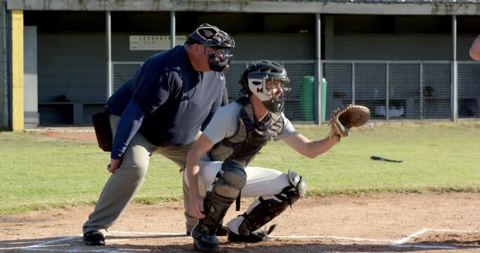 Upon umpire signaling male catcher at home plate catching ball in mitt securing strike