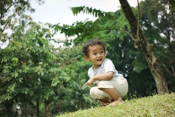 Happy boy enjoying nature in a green and lush outdoor garden while learning to explore with his hand gesture pointing towards the grass.