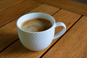 A simple, inviting shot of a white ceramic mug of coffee with foam on a wooden table 1