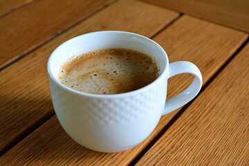 A simple, inviting shot of a white ceramic mug of coffee with foam on a wooden table 2