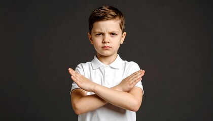 Boy crossing arms with disapproval, refusing, saying no, serious expression, and gray background.