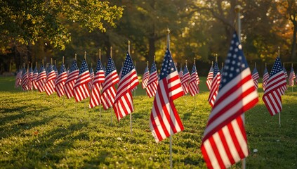 A field of american flags waving in the wind on a sunny day in a park with trees in the background