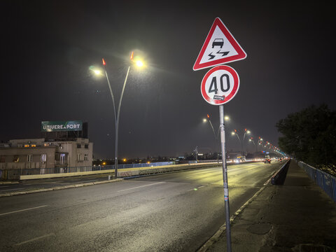 BELGRADE, SERBIA - APRIL 22, 2025: Night view of Brankov Most bridge in Belgrade with a speed limit and slippery road warning posted on a wet roadway, illustrating urban driving conditions.
