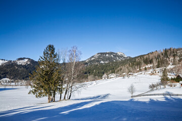 Panoramic view of Zgornje Jezersko, an alpine village in Slovenia Julian Alps. Snow covers fields and farmhouses beneath forested slopes, on rural life and winter scenery in a quiet mountain valley.