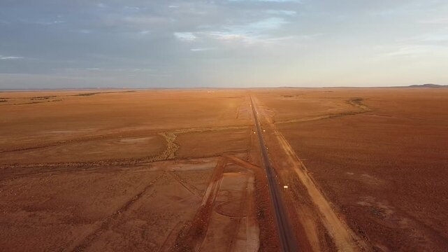 Drone photography of the dirt road from Quilpie to bedourie. An aerial shot of a long, straight, unsealed dirt road cutting through a vast, flat, and arid red desert landscape under a clear blue sky.