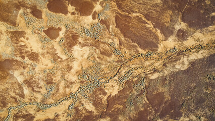 An aerial, abstract, top-down view of the ground in a desert landscape, showing textured patterns of light and dark. Drone photography of the desert inbetween Mount Isa and Boulia.