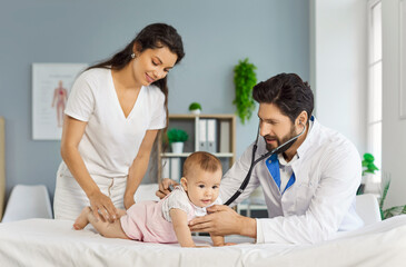 Friendly male pediatrician examining cute little baby with stethoscope lying on couch in medical clinic. Mother with child visiting doctor for examination in exam room. Medicine concept.