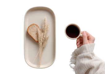 Light beige rectangular tray holds a slice of bread and wheat stalks, alongside a cup of coffee held by a hand in a cream-colored sweater