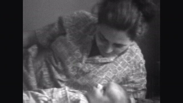 Close up, mother talking to cute newborn baby in room indoor. Old black and white family archives. Happy love memories. Mom lies near little infant. Maternity happiness. Vintage retro 1960s film
